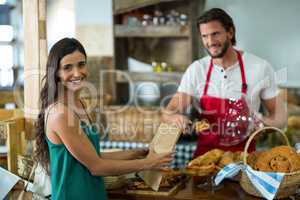 Smiling female customer receiving a parcel from bakery staff at counter