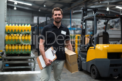 Factory staff holding cardboard box and clipboard in factory