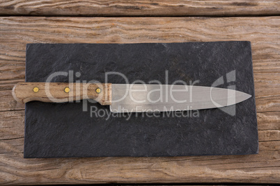 Knife on black slate board against wooden background