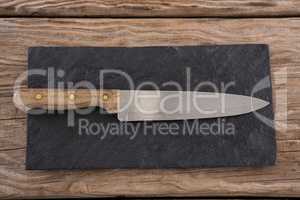 Knife on black slate board against wooden background