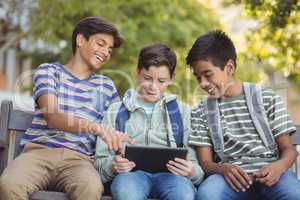 School kids using digital tablet on bench