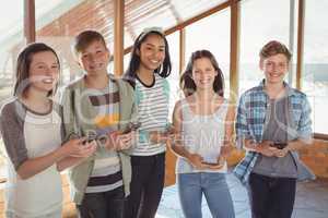 Portrait of smiling school friends using mobile phone in corridor