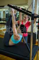 Female trainer assisting woman with stretching exercise on reformer