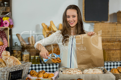 Portrait of smiling female staff putting croissant into a paper bag at counter