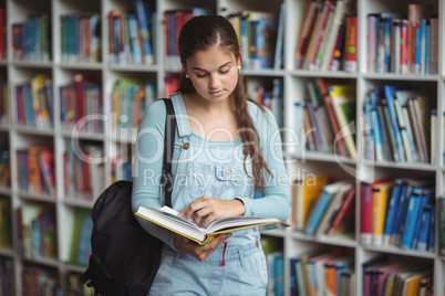 Attentive schoolgirl reading book in library