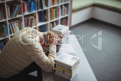 Tensed school teacher leaning on table in library