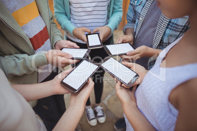 Mid section of school students standing in circle and using mobile phone