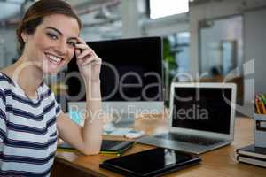 Smiling female graphic designer sitting at desk with digital tablet and laptop on table