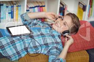 Schoolboy relaxing on couch while listening music on digital tablet in library