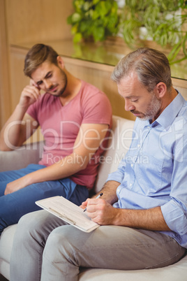 Doctor writing on clipboard while consulting patient