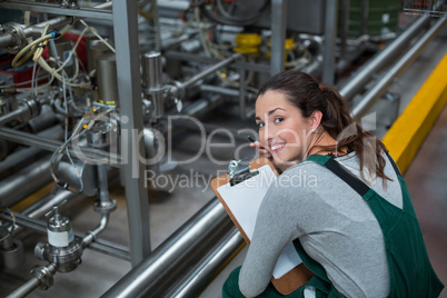 Female factory worker maintaining record on clipboard in factory