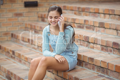 Happy schoolgirl sitting on staircase and talking mobile phone