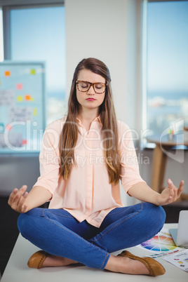 Female graphic designer sitting on table and meditating