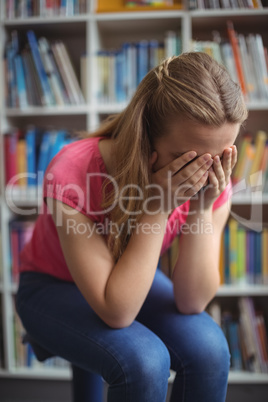 Sad schoolgirl sitting in library