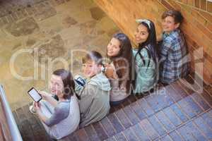 Portrait of smiling school friends sitting on staircase using mobile phone