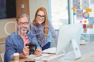 Portrait of male graphic designer holding digital camera with coworker