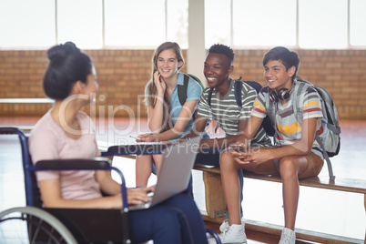 Disabled schoolgirl with classmates while using laptop in campus