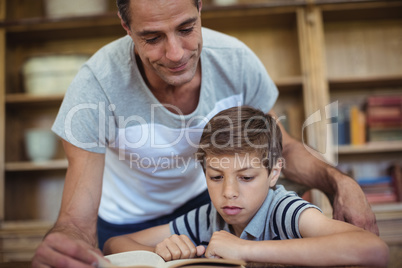 Father and son reading a book in study room