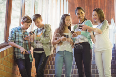 Group of smiling school friends using mobile phone in corridor