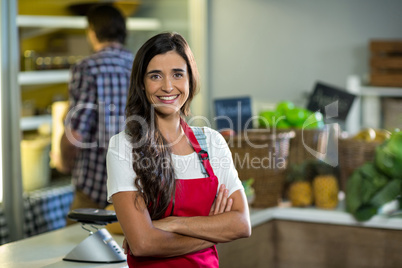 Smiling woman vendor standing at the counter in grocery store with arms crossed