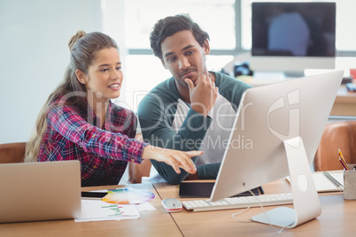 Male and female graphic designers discussing over computer