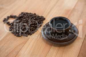 Cup of black coffee and coffee beans forming shape of cup