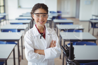 Portrait of schoolgirl standing with arms crossed in classroom