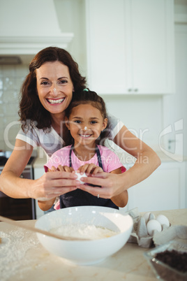 Mother and daughter breaking egg in bowl while preparing cookie