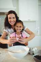 Mother and daughter breaking egg in bowl while preparing cookie