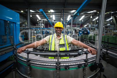 Portrait of smiling factory worker standing near the conveyor belt in factory