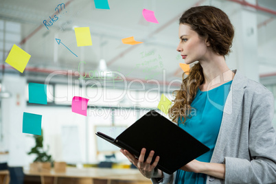 Female executive looking at sticky notes and holding folder