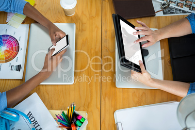 Female graphic designers using mobile phone and digital tablet on desk