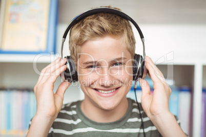 Portrait of happy schoolboy listening music on headphones in library