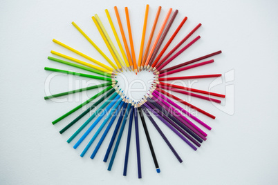 Colored pencils arranged in heart shape on white background