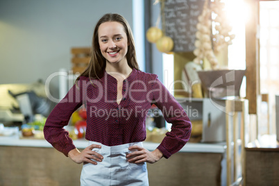 Portrait of smiling female staff standing with hands on hip against counter