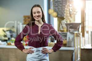 Portrait of smiling female staff standing with hands on hip against counter