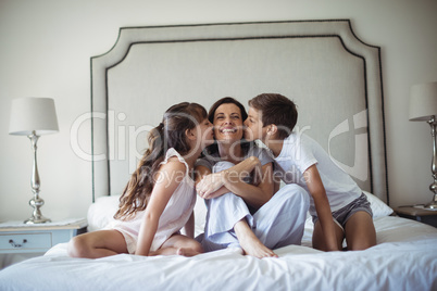 Kids kissing their mother on cheek in bedroom