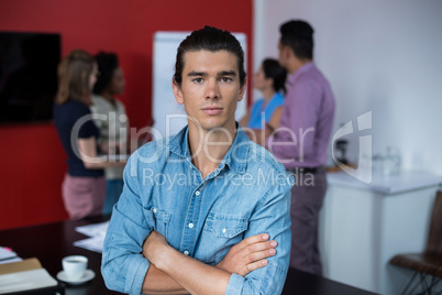 Portrait of business executive standing with arms crossed at meeting