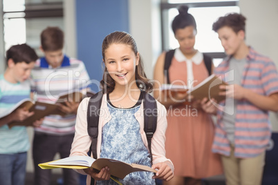 Portrait of smiling schoolgirl standing with book in classroom