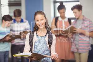 Portrait of smiling schoolgirl standing with book in classroom