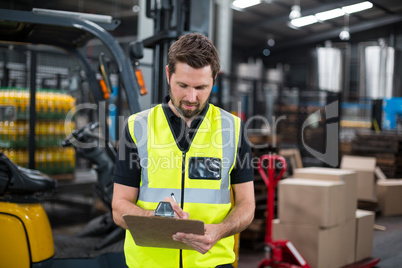 Factory worker writing on clipboard in factory