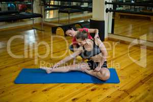 Female trainer assisting woman with exercise