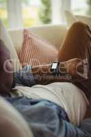 Man lying on sofa and checking his smartwatch