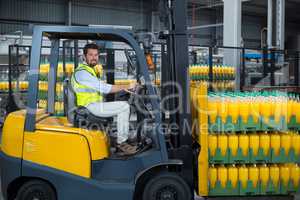 Factory worker loading packed juice bottles on forklift in factory