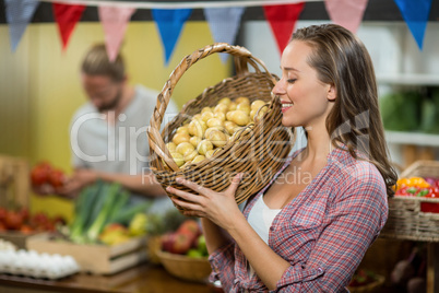 Woman vendor holding a basket if potatoes in grocery store