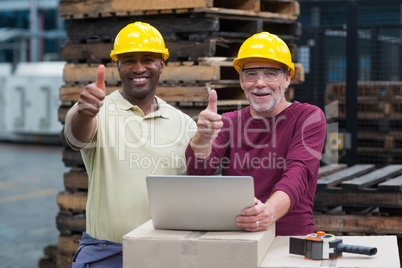 Two factory workers with laptop showing their thumbs up in drinks production plant