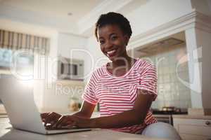 Portrait of smiling woman using laptop in kitchen