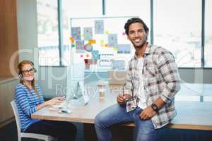 Male graphic designer sitting on desk with coworker in conference room