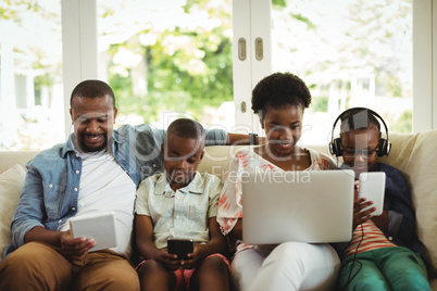 Parents and kids using laptop, smartphone and digital tablet on sofa