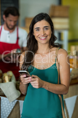 Portrait of smiling woman using mobile phone at counter